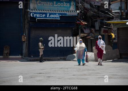 Srinagar, Indien. Mai 2021. Kaschmirische Frauen, die Gesichtsmasken tragen, als Vorsichtsmaßnahme gegen die Ausbreitung von Covid-19, laufen an einem indischen paramilitärischen Soldaten vorbei, der während der Beschränkungen in Lal chowk auf einem geschlossenen Markt wachsam ist.die Behörden haben am Freitag die Ausgangssperre Covid-19 im Bezirk Srinagar am Vorabend des Todestages von Mirwaiz Molvi verschärft Mohammad Farooq und Abdul Ghani Lone, die am 21. Mai in Kaschmir markiert werden. Kredit: SOPA Images Limited/Alamy Live Nachrichten Stockfoto