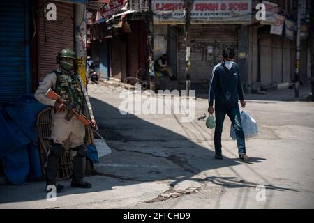 Srinagar, Indien. Mai 2021. Ein Mann mit Gesichtsmaske als Vorsichtsmaßnahme gegen die Ausbreitung von Covid-19 kommt während der Beschränkungen in Lal chowk an einem paramilitärischen Soldaten Indiens vorbei.die Behörden haben am Freitag die Ausgangssperre von Covid-19 im Bezirk Srinagar am Vorabend des Todestages von Mirwaiz Molvi Mohammad Farooq und Abdul Ghani verschärft Lone, das am 21. Mai in Kaschmir markiert wird. Kredit: SOPA Images Limited/Alamy Live Nachrichten Stockfoto