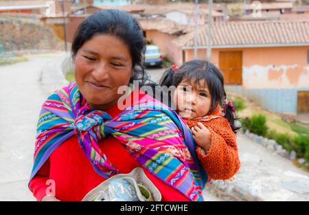 Eine lokale Quechua-Frau trägt ihre Tochter in einem Schal-Papoose in Chinchero, einem rustikalen Andendorf im Heiligen Tal, Urubamba, Cusco, Peru Stockfoto