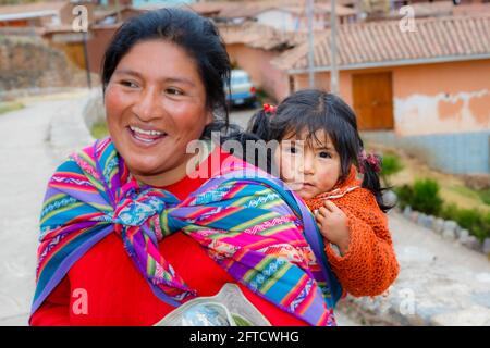 Eine lokale Quechua-Frau trägt ihre Tochter in einem Schal-Papoose in Chinchero, einem rustikalen Andendorf im Heiligen Tal, Urubamba, Cusco, Peru Stockfoto