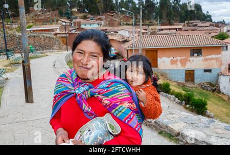 Eine lokale Quechua-Frau trägt ihre Tochter in einem Schal-Papoose in Chinchero, einem rustikalen Andendorf im Heiligen Tal, Urubamba, Cusco, Peru Stockfoto