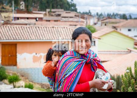 Eine lokale Quechua-Frau trägt ihre Tochter in einem Schal-Papoose in Chinchero, einem rustikalen Andendorf im Heiligen Tal, Urubamba, Cusco, Peru Stockfoto