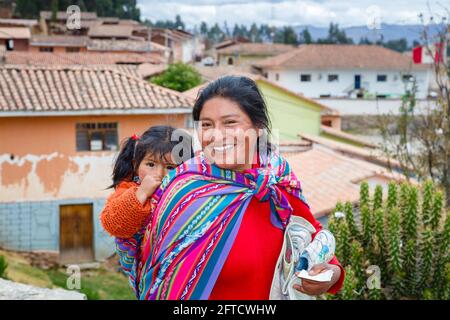 Eine lokale Quechua-Frau trägt ihre Tochter in einem Schal-Papoose in Chinchero, einem rustikalen Andendorf im Heiligen Tal, Urubamba, Cusco, Peru Stockfoto