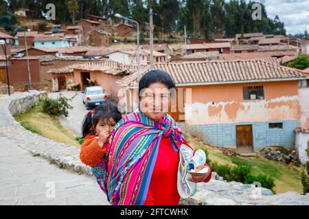 Eine lokale Quechua-Frau trägt ihre Tochter in einem Schal-Papoose in Chinchero, einem rustikalen Andendorf im Heiligen Tal, Urubamba, Cusco, Peru Stockfoto