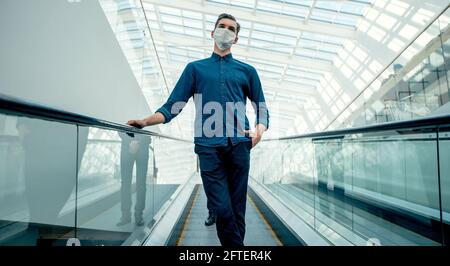Junger Mann in einer Schutzmaske, der auf der Rolltreppe steht. Stockfoto