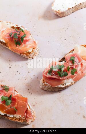 Baguette-Scheiben mit Schlagsahne, Serrano-Schinken und Mikrokräutern. Stockfoto