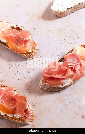 Baguette-Scheiben mit Schlagsahne, Serrano-Schinken und gerissenem Pfeffer. Stockfoto