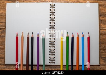 Offenes Notizbuch mit weißen Blättern auf dem Tisch und vielen Buntstifte am unteren Rand aufgereiht Stockfoto