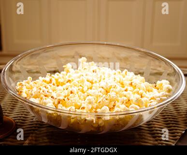 Klar gemusterte Schale mit frisch gepopptem Popcorn auf Glastisch Mit einer Flasche Limonade aus Glas und einer Fernbedienung im fernseher Beide Seiten mit Schränken im Hintergrund Stockfoto