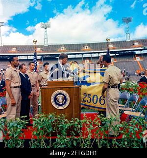 Präsident John F. Kennedy erhält die Flagge der 2506. Kubanischen Invasionsbrigade von Brigade-Mitgliedern während einer feierlichen Präsentation im Orange Bowl Stadium in Miami, Florida. Auf dem Rednerpult (von links nach rechts): Erneido Oliva, zweiter Kommandant der Brigade; Robert King High, Bürgermeister von Miami; Jose Pérez San Román, Kommandeur der Brigade; Manuel Artime, Zivilchef der Brigade; Präsident Kennedy (am Rednerpult mit Flagge); Dolmetscher des US-Außenministeriums, Donald Barnes (meist hinten versteckt, mit Flagge); First Lady Jacqueline Kennedy – teilweise hinter Flagge versteckt. Stockfoto