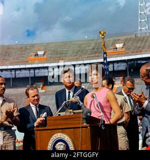 First Lady Jacqueline Kennedy hält bei einer Zeremonie der 2506. Flagge der kubanischen Invasionsbrigade im Orange Bowl Stadium in Miami, Florida, Bemerkungen auf Spanisch; Mitglieder der Brigade überreichten ihre Flagge an Präsident John F. Kennedy und Frau Kennedy. Auf der Rednerplattform (von links nach rechts): Erneido Oliva, zweiter Kommandant der Brigade (applaudierende); Bürgermeister von Miami, Robert King High (applaudierende); Präsident Kennedy; Jose Pérez San Román, Kommandant der Brigade (hinten, meist versteckt); die First Lady (an Rednermikrofonen); Manuel Artime, Chef der zivilen Brigade . Stockfoto