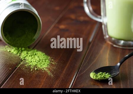 Matcha-Getränk und Pulver auf dunklem Holz; japanischer grüner Tee; Servieren; Matcha auf Löffel; Tasse grüner Matcha-Tee Stockfoto