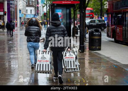 London, Großbritannien. 21 Mai 2021. Menschen, die im Regen in der Oxford Street einkaufen. Das Office for National Statistics (ONS) hat berichtet, dass die Einzelhandelsumsätze im April um 10 % über dem Stand vor der Pandemie lagen, wobei der Absatz von Kleidung im Vergleich zum März um 70 % gestiegen ist. Es wurde vermutet, dass der Anstieg ein Beleg für die aufgestaute Nachfrage ist, da am 12. April in England wieder Geschäfte eröffnet wurden, die nicht unbedingt notwendig sind. Kredit: Stephen Chung / Alamy Live Nachrichten Stockfoto