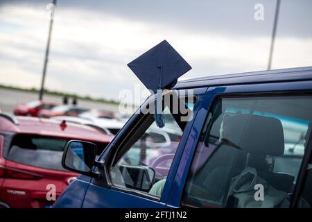 Bremerhaven, Deutschland. Mai 2021. Ein Absolvent winkt aus einem Auto einen Doktorhut, während Absolventen der Hochschule Bremerhaven an einer Abschiedszeremonie und der Verleihung von Zertifikaten in Autos auf dem Willy-Brandt-Platz teilnehmen. Die Teilnehmer konnten die Zeremonie vom Auto aus auf einer Bühne und über einen Bildschirm verfolgen. Quelle: Sina Schuldt/dpa/Alamy Live News Stockfoto