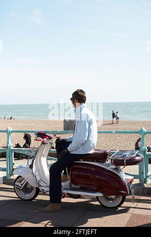 GROSSBRITANNIEN / England / Brighton / junger Mann sitzt auf seinem lambretta Roller neben dem Strand. Stockfoto