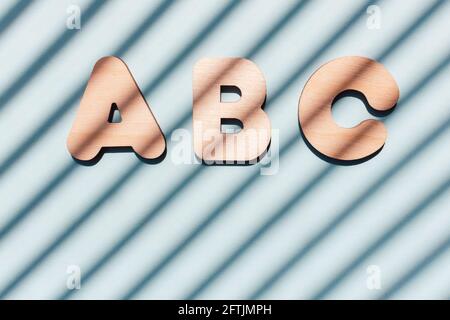 Inschrift ABC aus Holzbuchstaben. Das Konzept der Bedeutung von Bildung. Blauer Hintergrund mit diagonalen Schatten. Stockfoto
