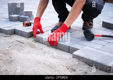 Der Meister in gelben Handschuhen legt Pflastersteine Stockfoto