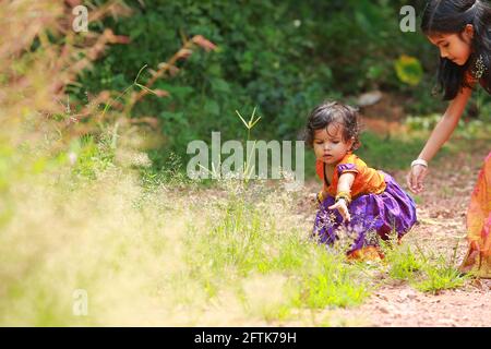 Südindische Mädchen Kinder tragen schöne traditionelle Kleid langen Rock und Bluse, Zupfen der Blumen von welligem Haar Gras, Grün Hintergrund. Stockfoto