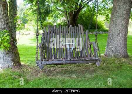 Hausgemachtes Holz schwingen im Sommer zwischen Bäumen in parkähnlicher Umgebung. Dieses Loveseat Naturmöbel wurde aus Ästen und Stäben hergestellt. Perfekt Stockfoto