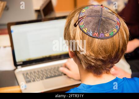 Junger jüdischer Junge in farbenfroher hebräischer Yarmulke von hinten, der in der Schule auf einer Tastatur tippt. Stockfoto