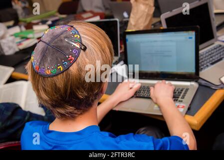 Junger jüdischer Junge, der in der Schule Yarmulke von hinten trägt und auf einer Tastatur tippt. Stockfoto