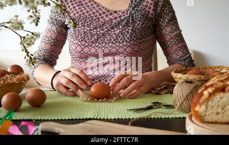 Frau, die zu Hause Ostereier zum Färben mit Zwiebelschalen zubereitet, im Vordergrund Blumen und mazanec-Gebäck Stockfoto