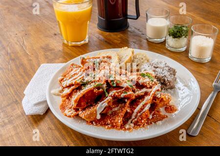 Mexikanische traditionelle Chilaquiles Frühstück Grüne rote Salsa Orangensaft aus Holz Stockfoto