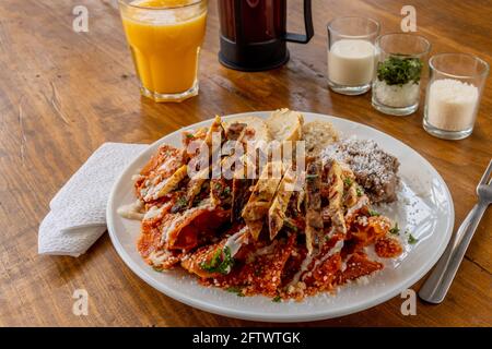 Mexikanische traditionelle Chilaquiles Frühstück Grüne rote Salsa Orangensaft aus Holz Stockfoto