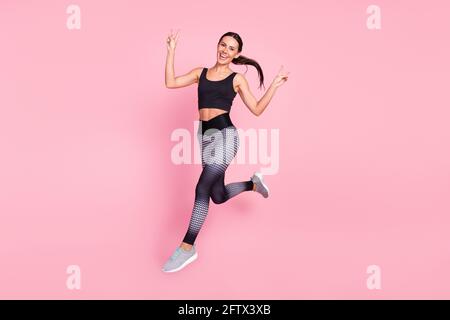 Ganzkörper-Profil Seitenfoto der jungen sportlichen Frau glücklich Smile Run Jump zeigen Frieden cool V-Zeichen isoliert über Pastell Farbiger Hintergrund Stockfoto