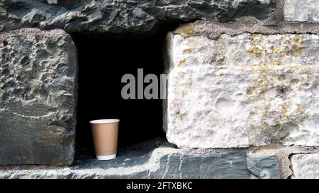 Der Papierbecher wurde als Müll in der alten Steinmauer zurückgelassen Stockfoto