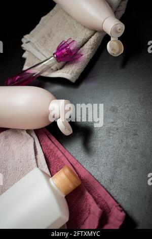 Einige rosa Handtücher und einige weiße Flaschen auf einem schwarzen Holztisch in einem Spa Stockfoto