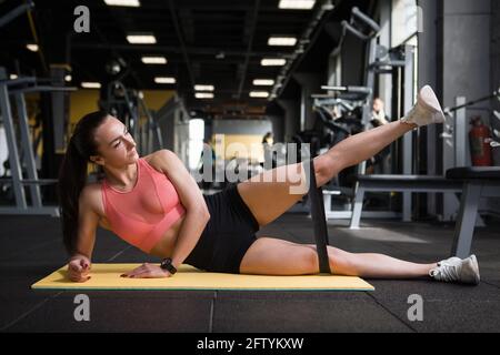 Junge Fitness-Frau tut Widerstand Band Bein hebt an der Fitnessraum Stockfoto