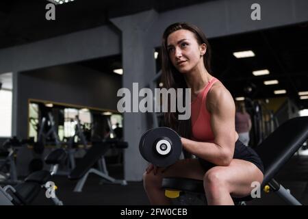 Sportlerin mit muskulösen Armen, die Bizeps-Locken macht, im Fitnessstudio, Platz kopieren Stockfoto