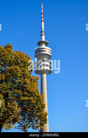 München, Deutschland - 25 2012. Oktober: Fernsehturm von München im Olympiapark hinter herbstlichen bunten Bäumen unter sonnenblauem Himmel Stockfoto