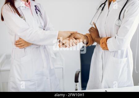 Gesundheitswesen, Vereinbarung und Einstellungskonzept. Zwei nicht erkennbare professionelle multirassische verschiedene weibliche Doktoren Händeschütteln im modernen Krankenhaus, die Hände aus der Nähe Stockfoto