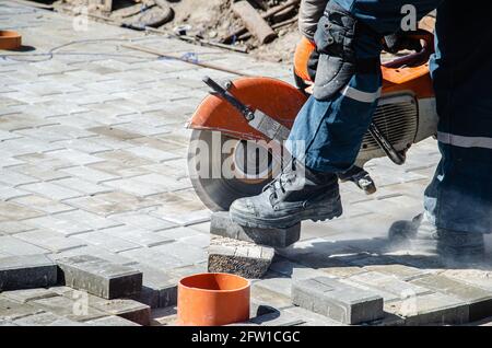 Ein Arbeiter schneidet Pflasterplatten mit einem Gasschneider und Eine Handsäge Stockfoto