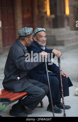 Zwei alte Männer sitzen mit Spazierstöcken und unterhalten sich auf einer Kashgar-Straße Kashgar, Xinkiang, Volksrepublik China, 2019 Stockfoto