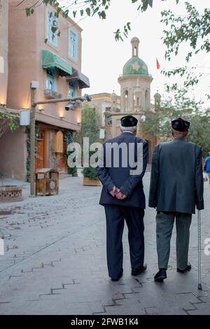 Zwei ältere Männer mit traditionellem Uyhgur-Hut gehen in der Nähe der Moschee. Kashgar, Xinkiang, Volksrepublik China, 2019 Stockfoto