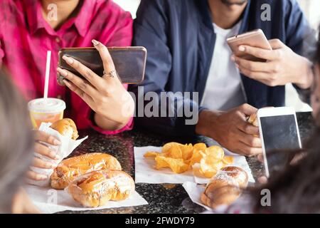 Eine Gruppe von nicht erkennbaren Menschen, die mit dem Handy beschäftigt sind, während sie gemeinsam im Restaurant Snacks essen – Konzept der Millennials, die Junk-Food und Telefonabhängigkeit haben Stockfoto