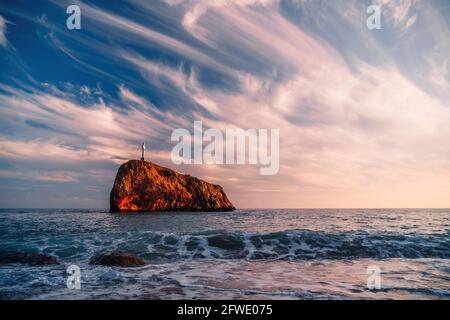 Heller Sonnenuntergang am Meer. Die Wellen stürzen in den Felsen, erleuchtet von dem warmen Sonnenuntergang, Sand und Kieselsteinen, vulkanischem Basalt wie in Island. Meereswelle bricht in Stockfoto