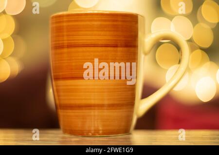 Kaffeetasse auf Holztisch mit verwackelten Weihnachtslichtern im Hintergrund. Stockfoto