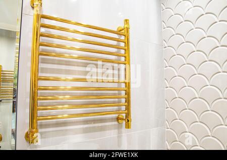 Goldener beheizter Handtuchhalter an einer weißen Wand, warmes Licht. Badezimmerwand Stockfoto