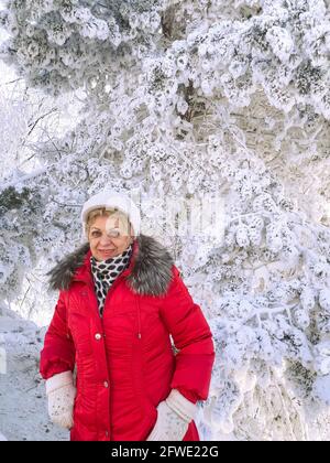 Lächelnde Frau, die den sonnigen Wintertag im verschneiten Wald genießt. Stockfoto