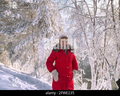 Lächelnde Frau, die den sonnigen Wintertag im verschneiten Wald genießt. Stockfoto