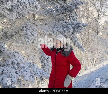 Lächelnde Frau, die den sonnigen Wintertag im verschneiten Wald genießt. Stockfoto