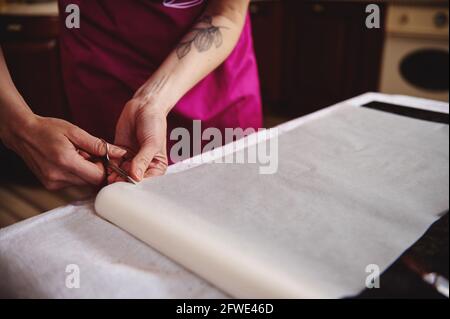 Konditor legt Backpapier aus, während er in der Küche steht. Nahaufnahme Stockfoto