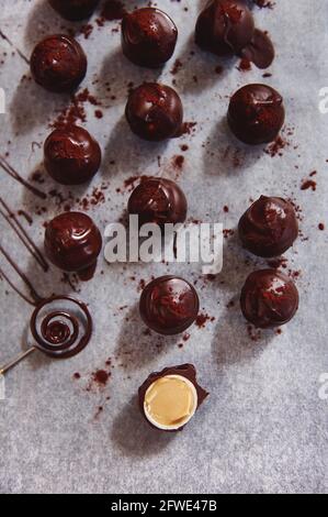 Flache Lay-Komposition mit Schokoladentrüffeln auf Backpapier und einem halbierten Schokoladenbonbon, gefüllt mit gesalzenem Karamell. Schokoladenwerkzeug liegt n Stockfoto