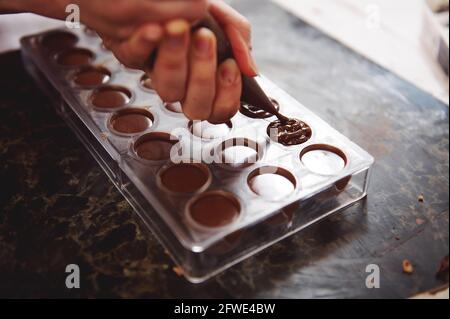 Konditor Füllung leere Schokoladenformen mit Füllung für die weitere Vorbereitung luxuriöse handgemachte Schokoladenprodukte. Nahaufnahme Stockfoto