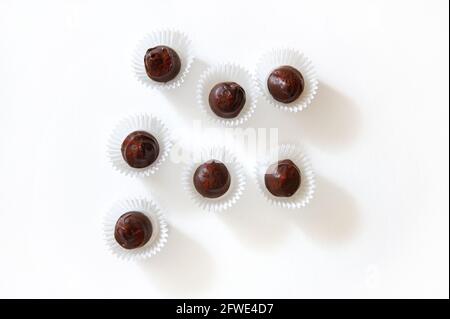 Flache Komposition aus Schokoladentrüffeln, bestreut mit gefriergetrockneten Erdbeeren in Papierverpackungen auf weißem Hintergrund mit Platz für Kopien. Konzept von Stockfoto