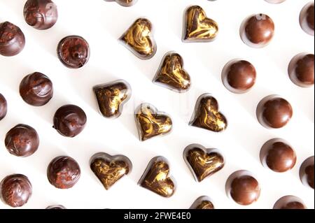 Flache Lay-Komposition mit einer Auswahl von handgefertigten belgischen Pralinen mit goldenem Ornament und Kakaopulver auf weißem Hintergrund. World Chocola Stockfoto